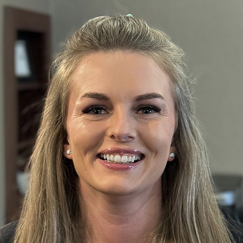 Smiling woman with long blonde hair and pearl stud earrings, indoors and well lit.