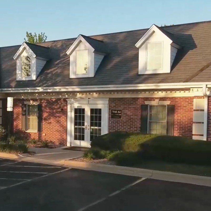 Single-story brick office building with three dormer windows on a sloped roof and a double glass entry door.